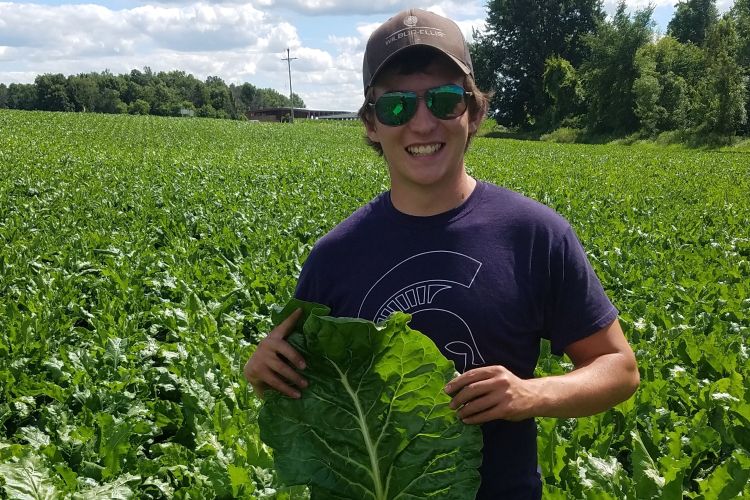 Recent crop and soil science grad Hans Bierlein is holding a lettuce leaf in a field.