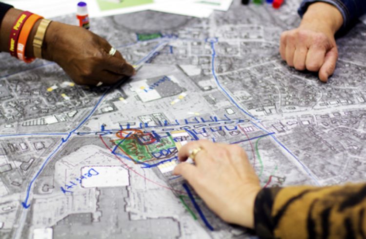 Photo of the hands of three people working together during a charrette on making design changes to a aerial map of a community.