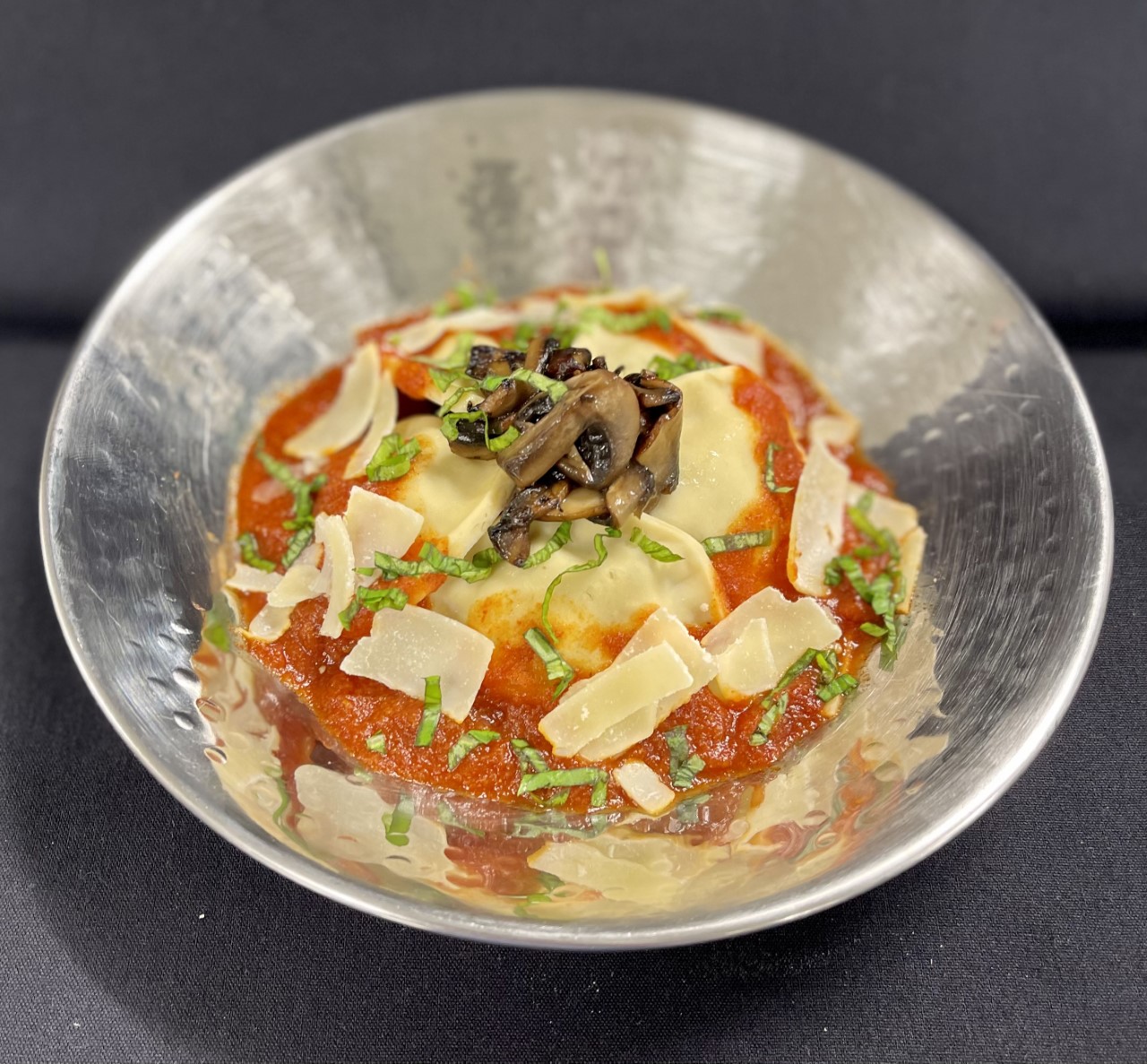 Ravioli with sauce, cheese and mushrooms in bowl.