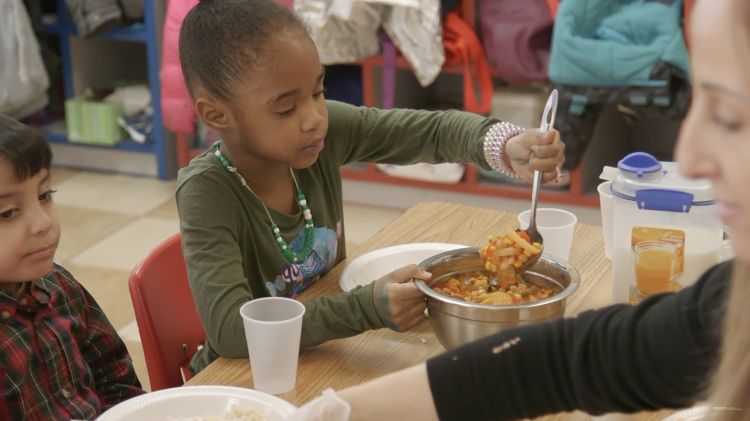 A child serves herself food at a table at a childcare center.