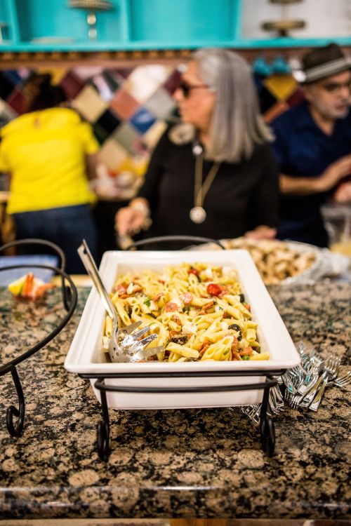 A dish of pasta left out on a table at a gathering, with people in the background.