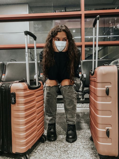A woman in a face mask sitting between luggage at an airport.