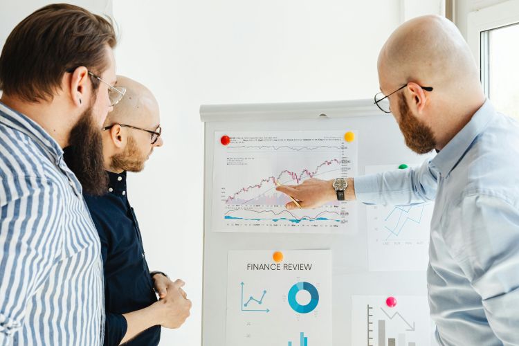 Three men standing around a large flip chart that shows various charts and graphs.
