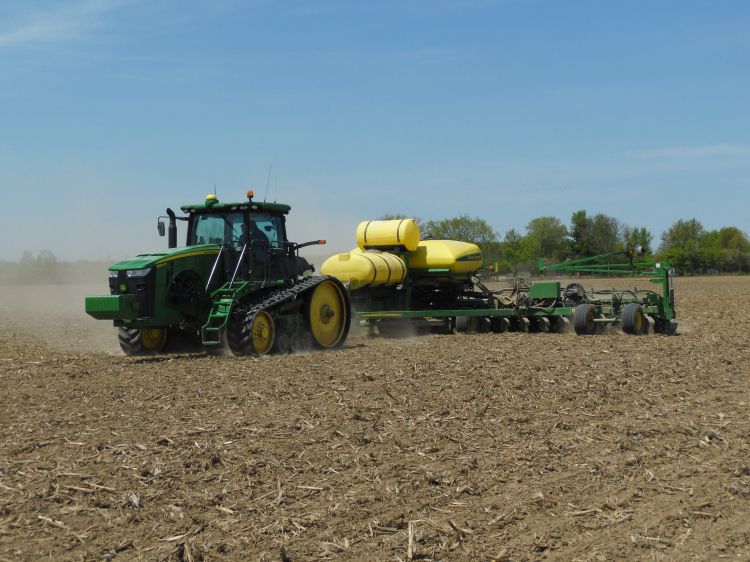 Tracked tractor pulling a planter across a harvested field.