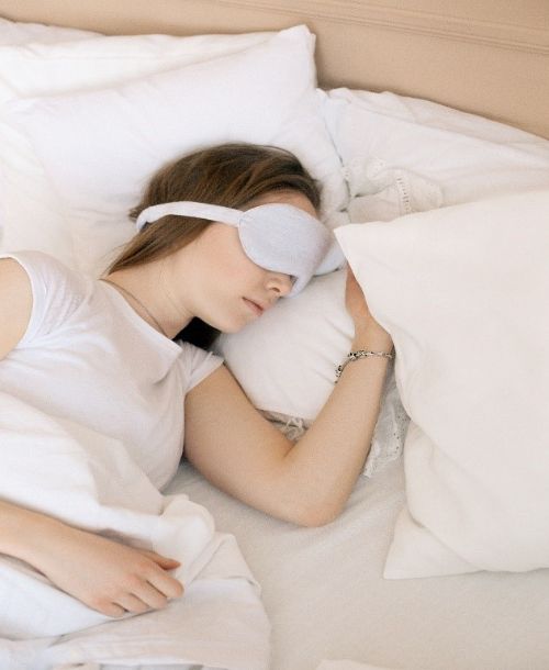A woman wearing a sleep mask over her eyes sleeping in a bed.