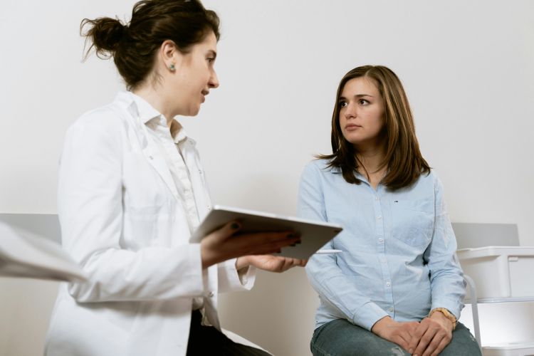 A doctor consults with a patient while holding a computer tablet in a waiting room.
