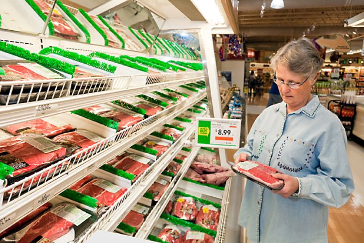 A woman looking at meat in a grocery store.