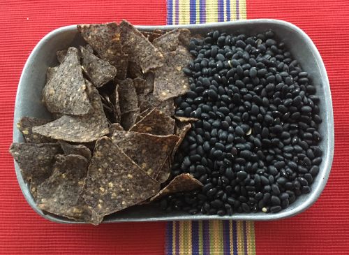 Bowl that is full of corn torilla chips and black beans.