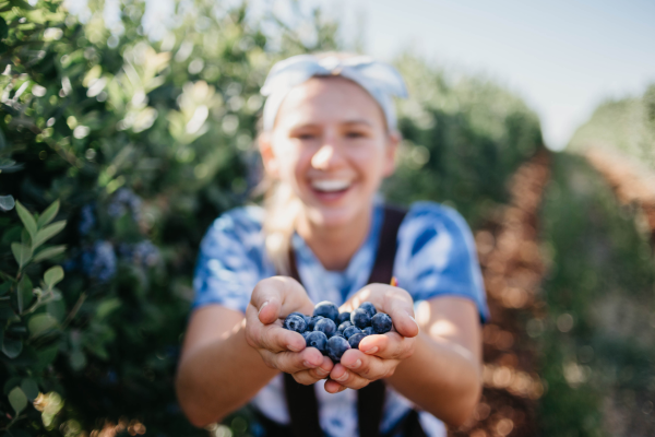 A young woman is smiling and holding blueberries in her hands.