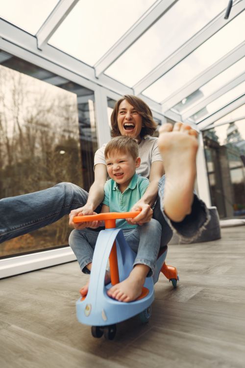 A woman playing on a toy scooter with a child.