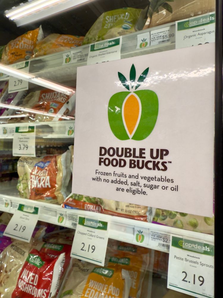 A photo of a promotional flyer for the Double Up Food Bucks program on a grocery store shelf in the frozen food aisle.