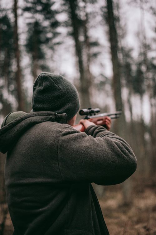 Man holding rifle in woods.