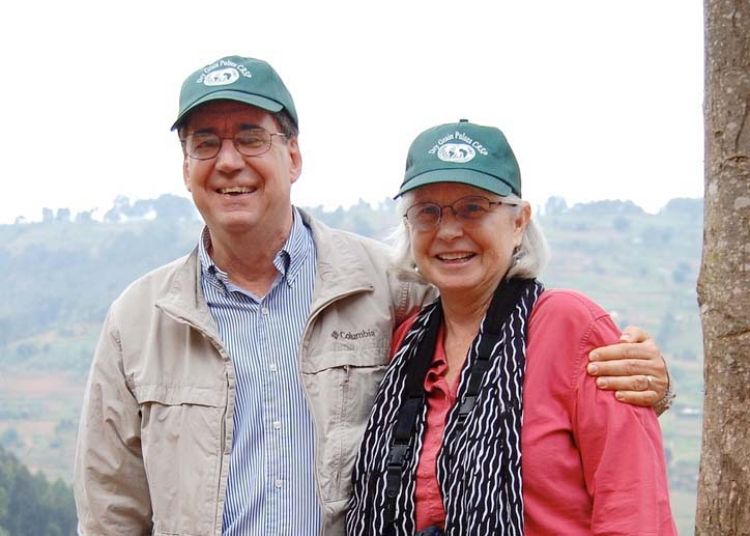 A photo of Irv Widders and Cynthia Donovan in the mountains of Rwanda. Both are wearing green baseball caps, and he has an arm around her. They are both smiling.