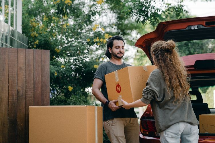 A young woman with long curly hair helping a young man lift a box into his car.