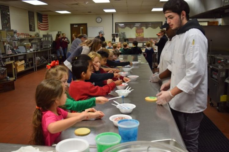 Young children in a cafeteria learning from chefs.