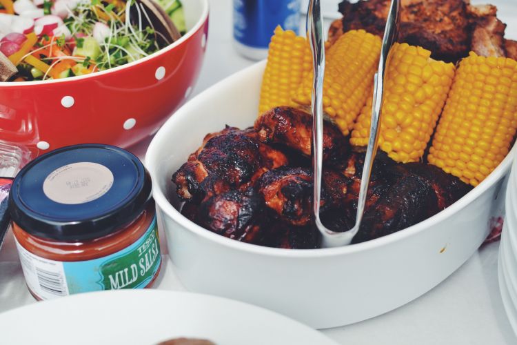 Grilled meat and corn dishes with salad on a table.