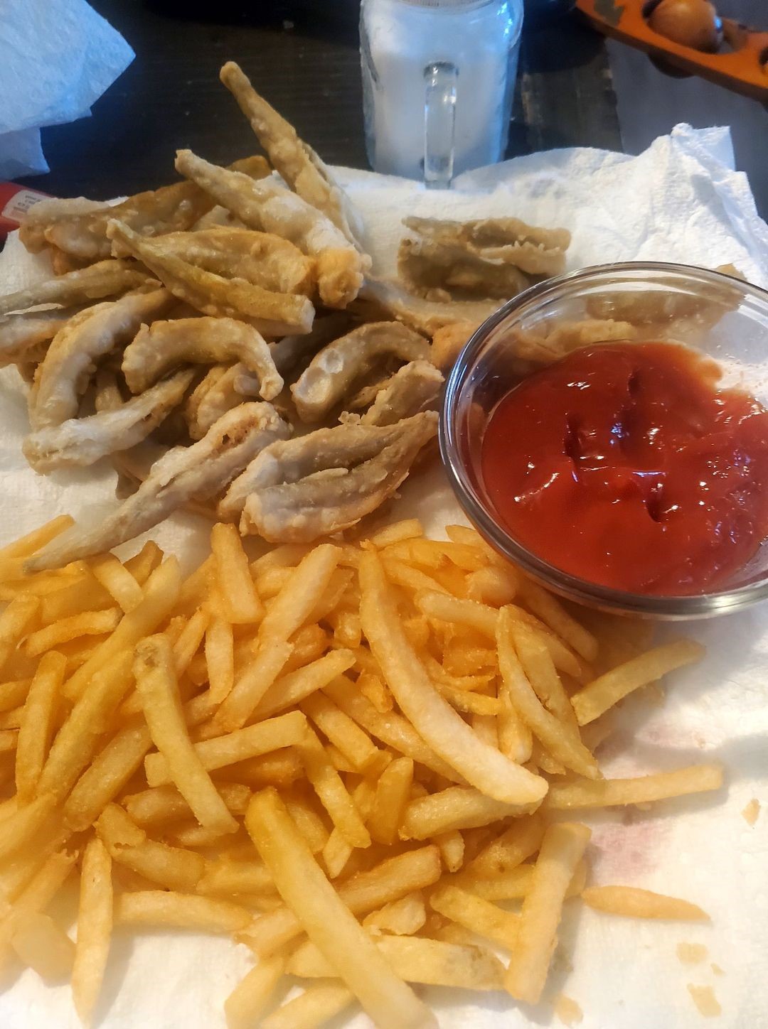A dinner plate holds fried smelt, french fries and a cup of ketchup.
