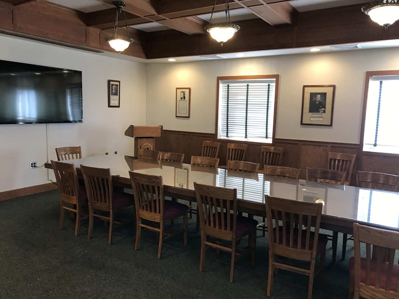 Conference room glass top table with chairs around it, tv and lectern in background, 
