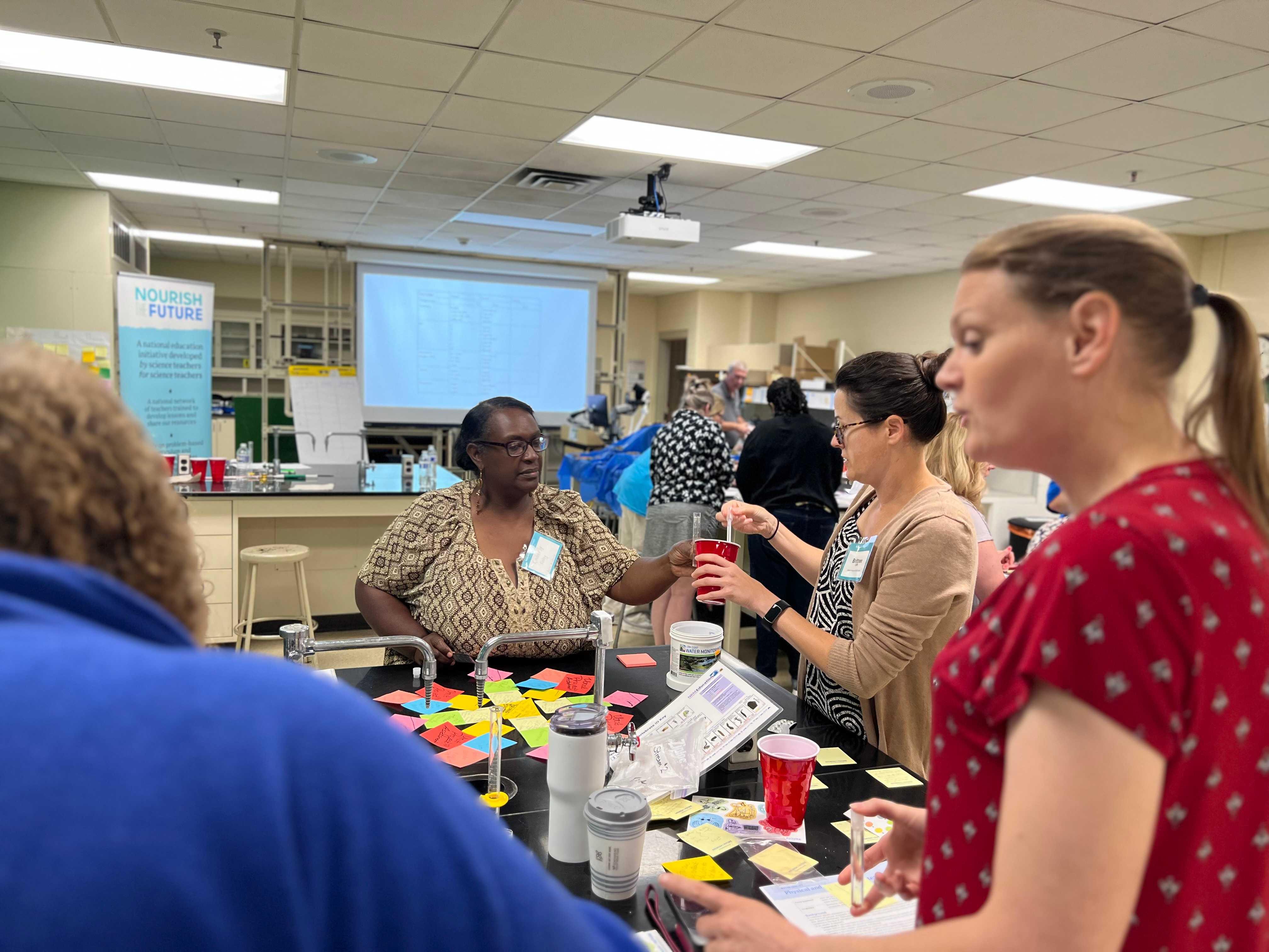 Teachers surround a lab bench cooperating on experiments. 