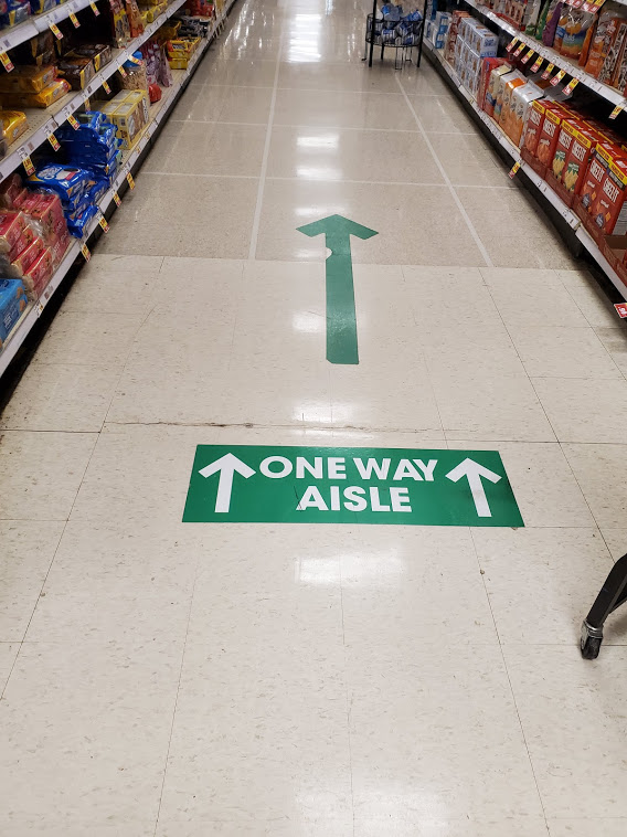 Grocery store aisle floor sign that reads "one way aisle" with arrows illustrating direction