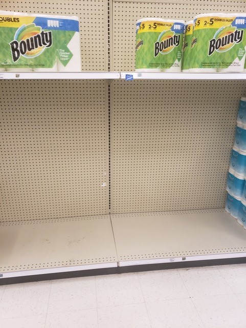 A few paper towel packages on a mostly empty grocery shelf