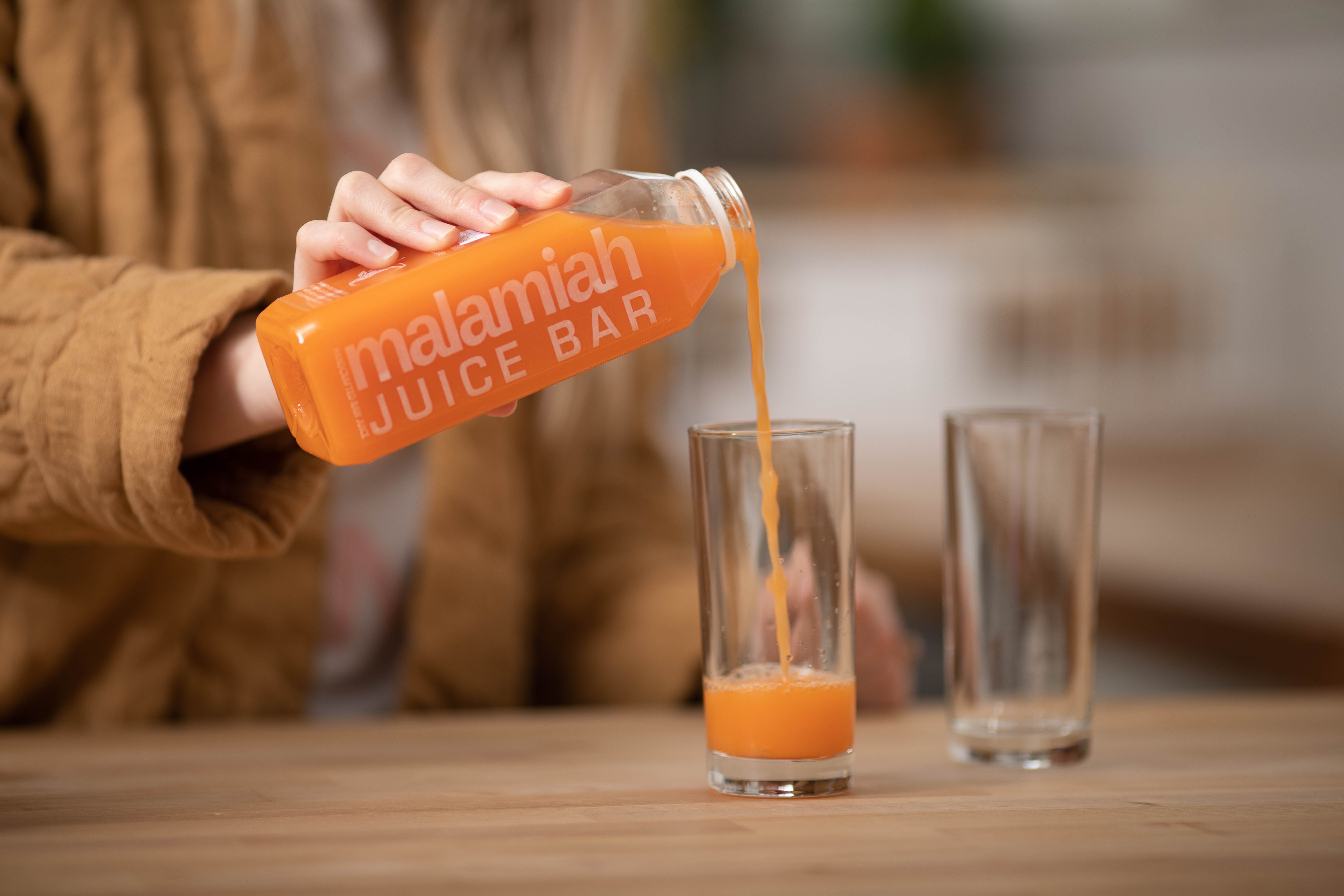 Person pours orange colored juice from Malamiah Juice Bar into a clear glass