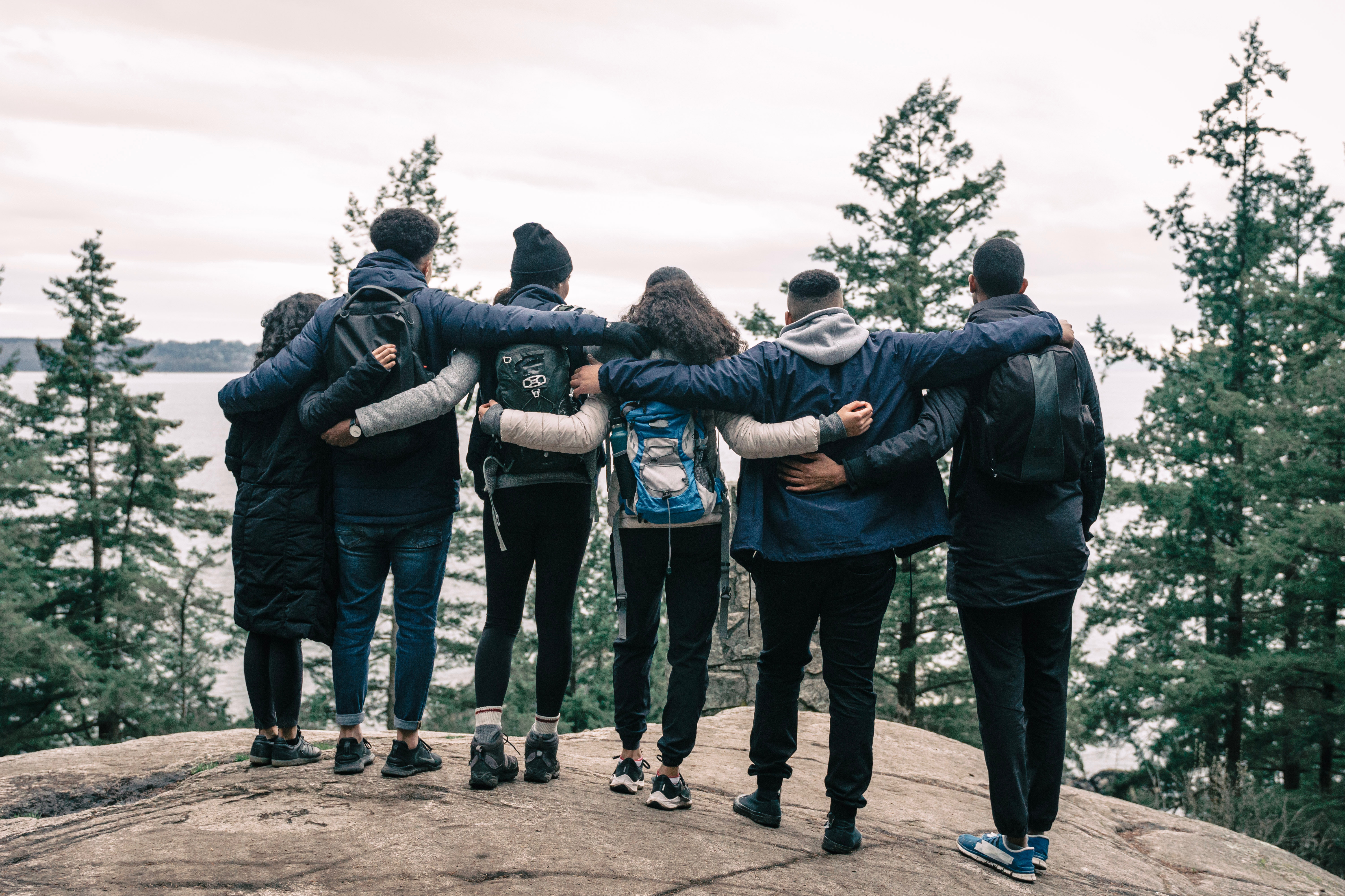 A picture of six individuals standing shoulder to shoulder with their arms around one another looking into the distance.