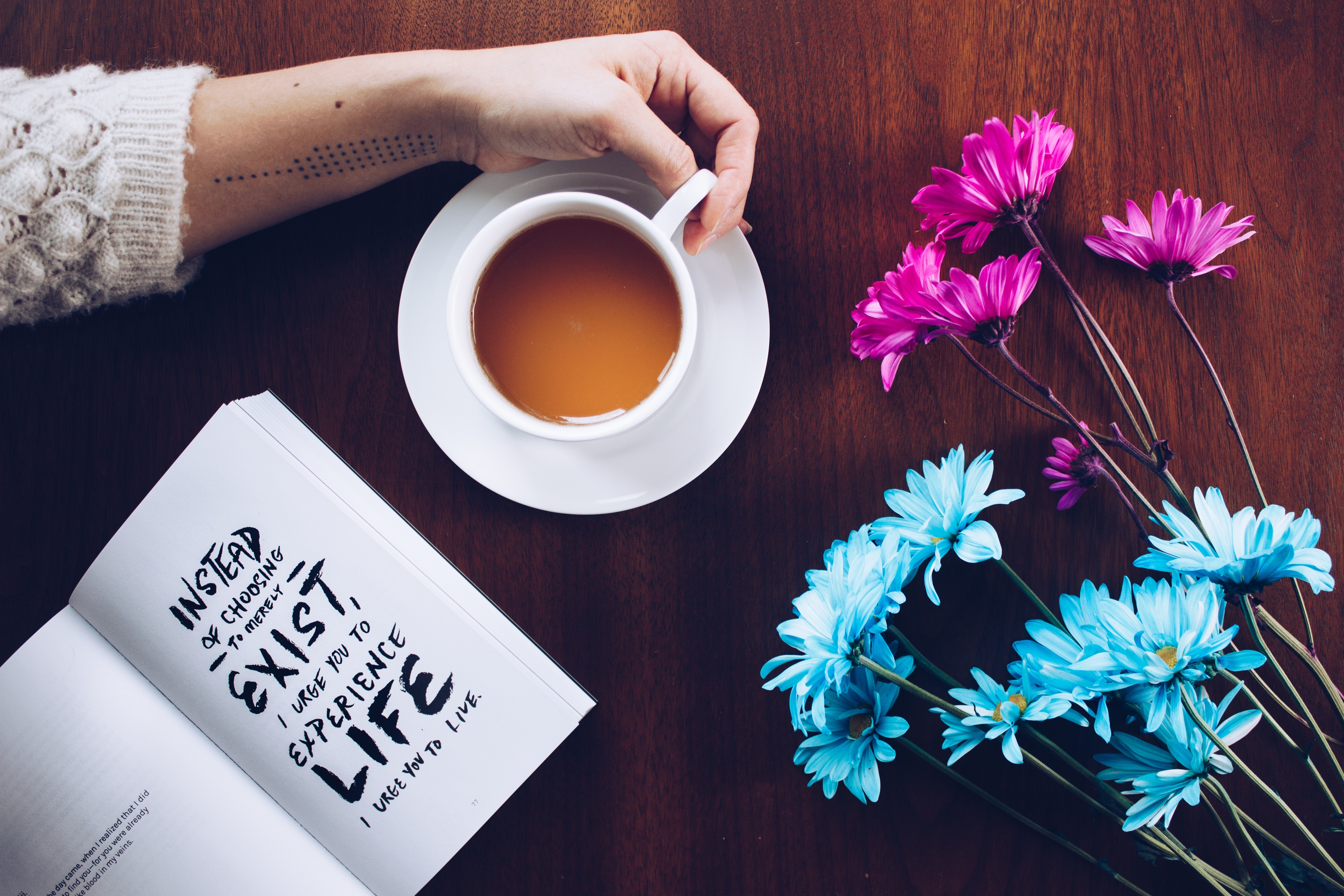 Picture of a cup of team a book and some flowers.