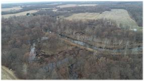 Progress photo of the Dowagiac River restoration site on March 18, 2022. Photo depicts the efforts to reshape the Dowagiac River, including a meandering river bend with banks covered by trees.