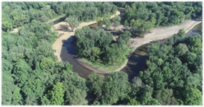 Progress photo of the Dowagiac River restoration site in September 2022. Photo depicts the efforts to reshape the Dowagiac River, including a meandering river bend with banks covered by trees.