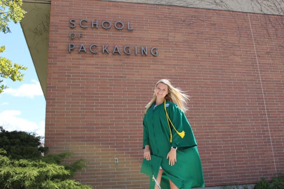 MSU student wearing cap and gown in front of MSU Packaging building