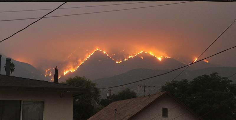 Fire in mountains in the distance with houses in the foreground.