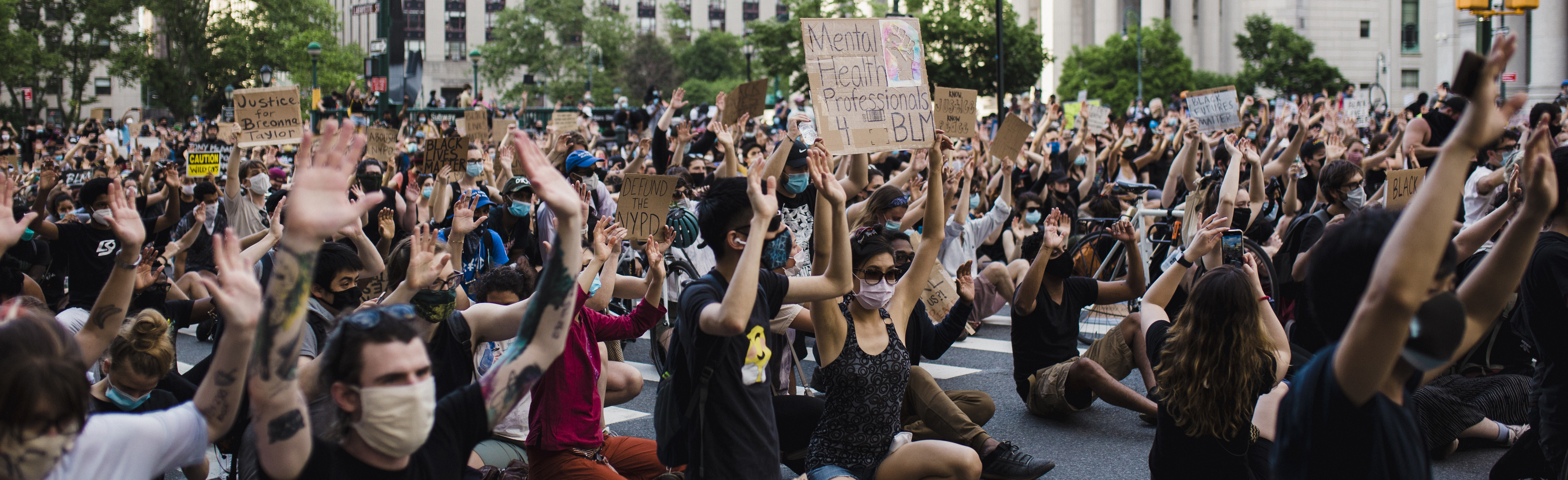Crowd of protesters wearing masks and holding signs and kneeling.