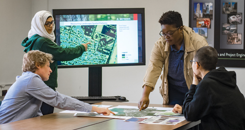 Environmental design graduate students meeting and discussing digital and hard-copy plan documents.