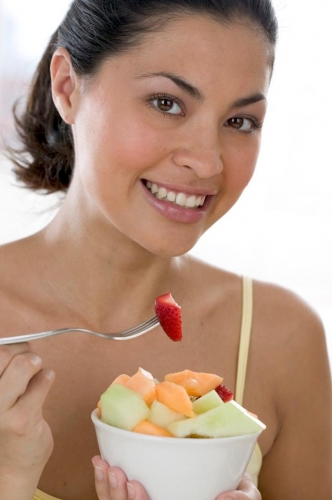 Woman eating a bowl of assorted melon.