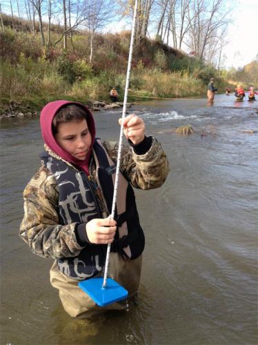 Male student collecting samples from a river image.