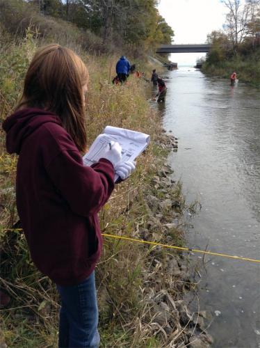 Girl taking notes by a river image.