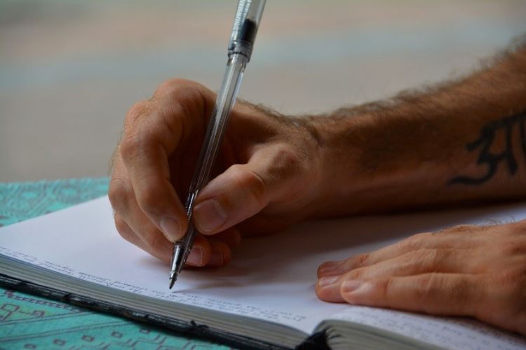 A close-up image of someone's hands as they write in a notebook with a pen.