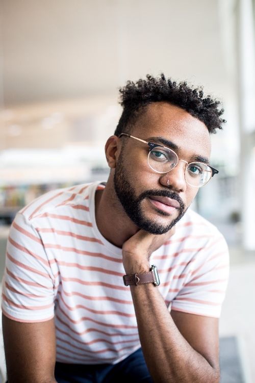 A portrait-style image of a young black man with glasses and a striped shirt.