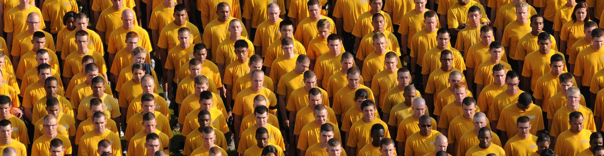 Group of men and women wearing yellow shirts standing shoulder to sholder in tight rows.